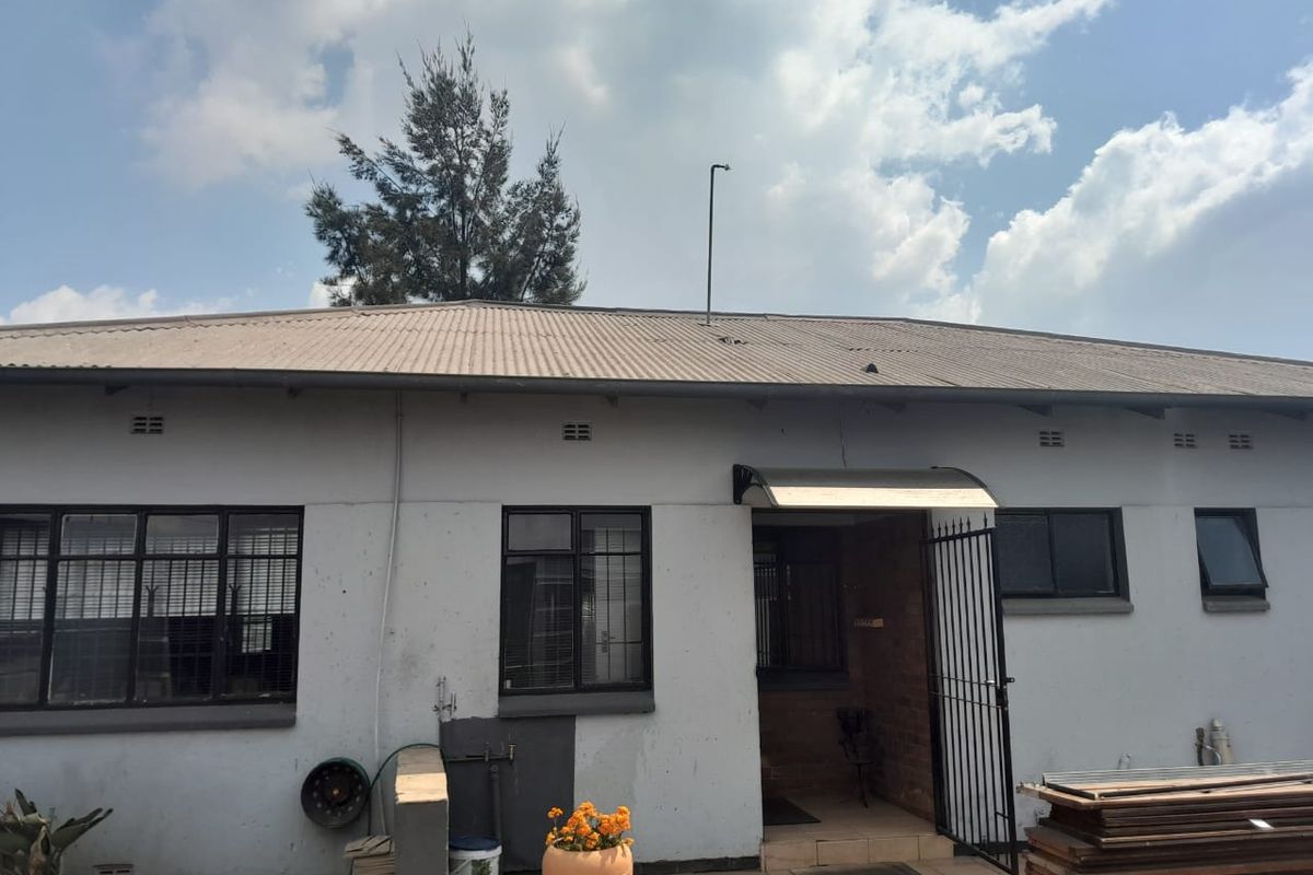 Rear exterior view of a commercial building featuring a corrugated metal roof, security gate, and tiled patio area with visible wall plaster cracks.