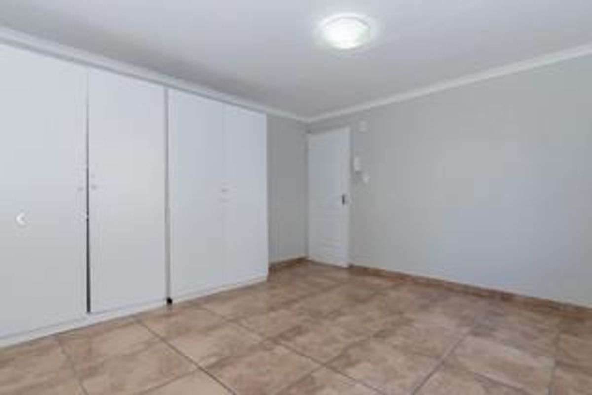 A clean, empty bedroom featuring neutral walls, tiled flooring, and ample built-in cupboard storage space.