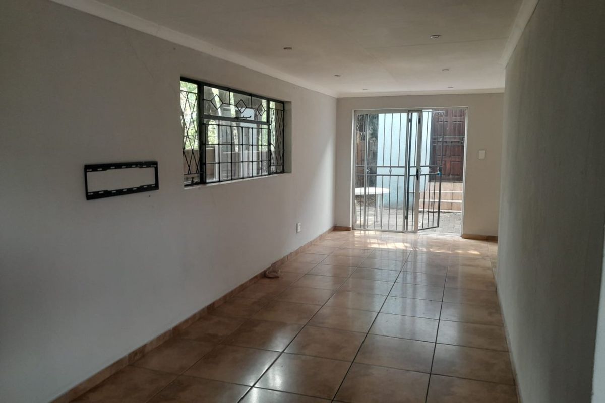 An empty, tiled living area featuring recessed lighting, security gates, and sliding glass doors leading to an outdoor space.