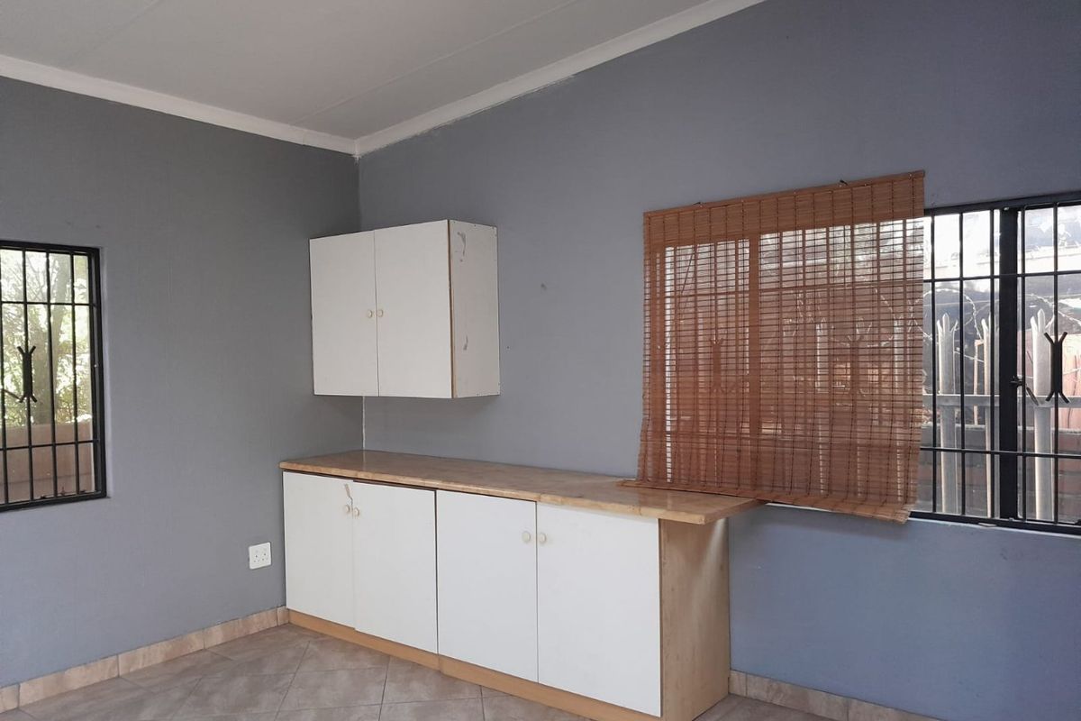 A functional kitchen area featuring white built-in cabinetry, laminate countertops, tiled flooring, and security bars on the windows.