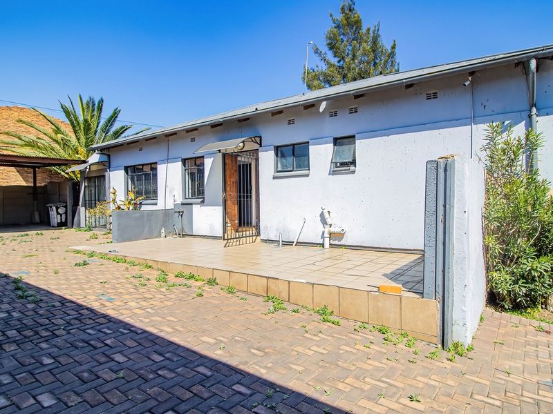 Rear exterior view of the commercial property featuring a tiled patio area, paved driveway, and security gate access.