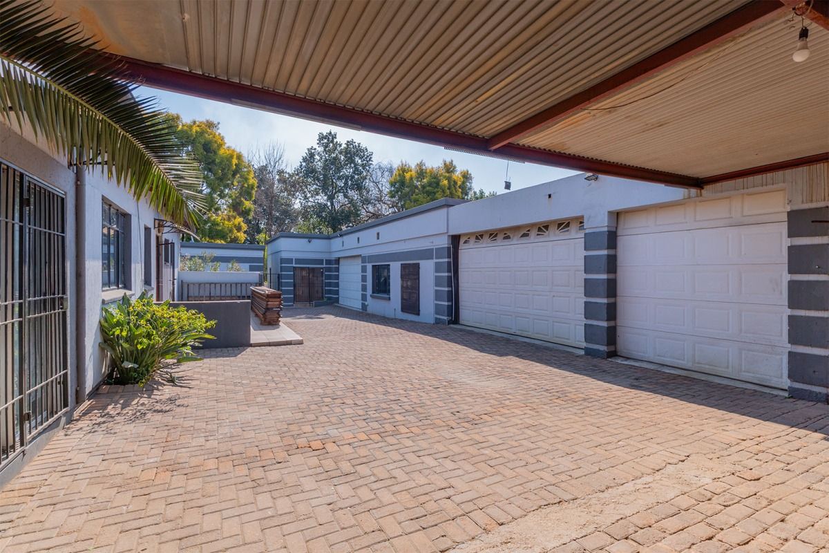 Rear exterior view featuring a paved driveway, covered parking area, and multiple garage access points with secure metal gates.