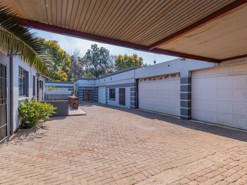 Rear exterior view featuring a paved driveway, covered parking area, and multiple garage access points with secure metal gates.