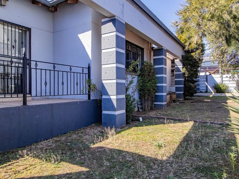 Rear exterior view of the commercial property featuring a covered patio area with security bars and concrete support pillars overlooking a garden space.