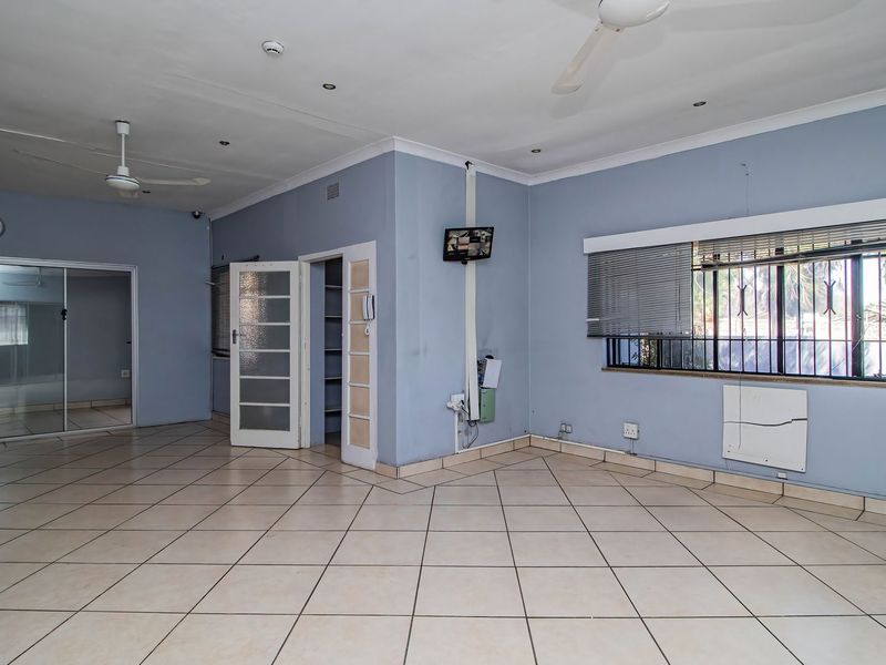 Spacious, empty living area featuring tiled flooring, ceiling fans, and security-fitted windows, offering a versatile blank canvas for commercial or office use.