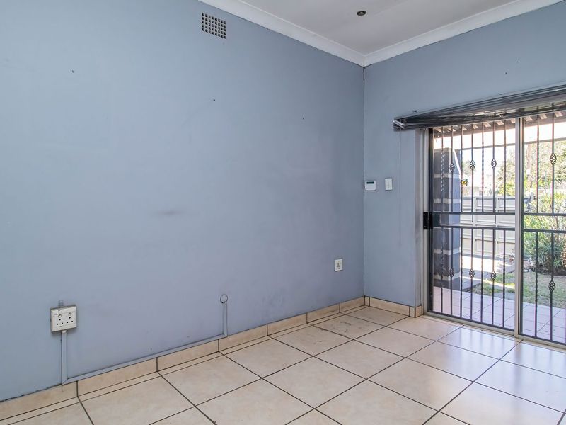 An empty living area featuring tiled flooring, recessed lighting, and a sliding glass door with a security gate leading to the exterior.