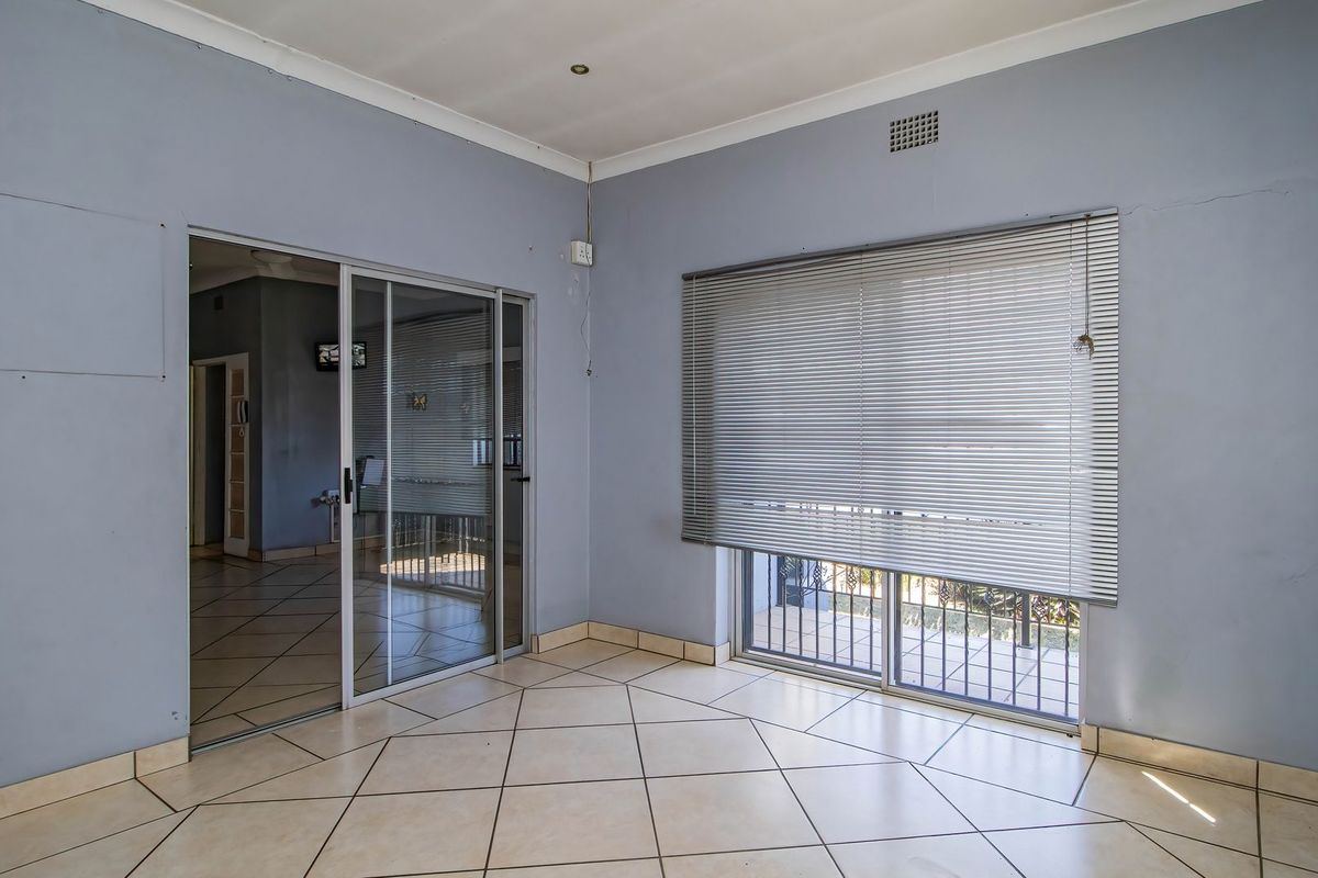 An empty living area featuring tiled flooring, sliding glass doors with venetian blinds, and neutral wall finishes, offering a versatile space for commercial use.