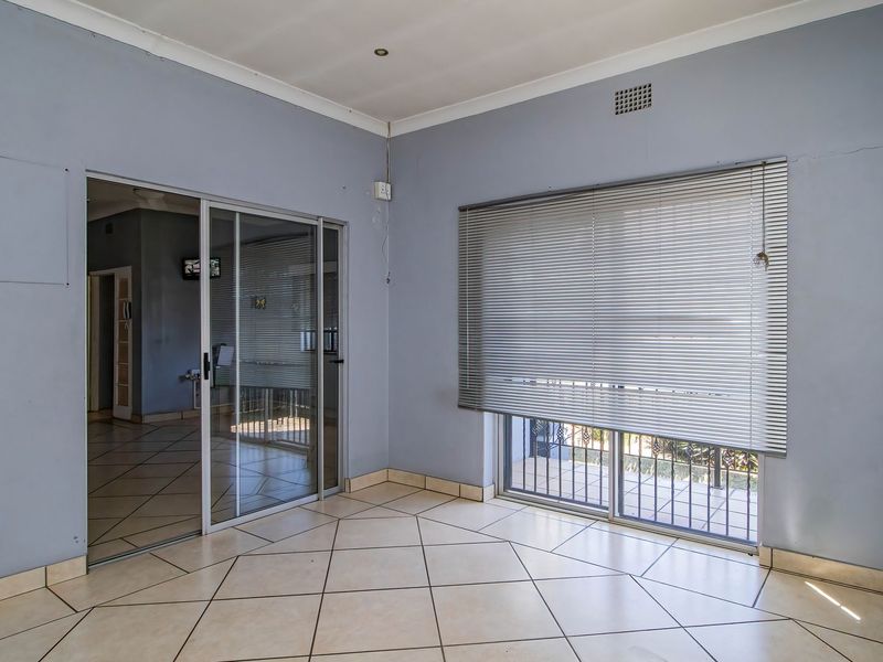 An empty living area featuring tiled flooring, sliding glass doors with venetian blinds, and neutral wall finishes, offering a versatile space for commercial use.