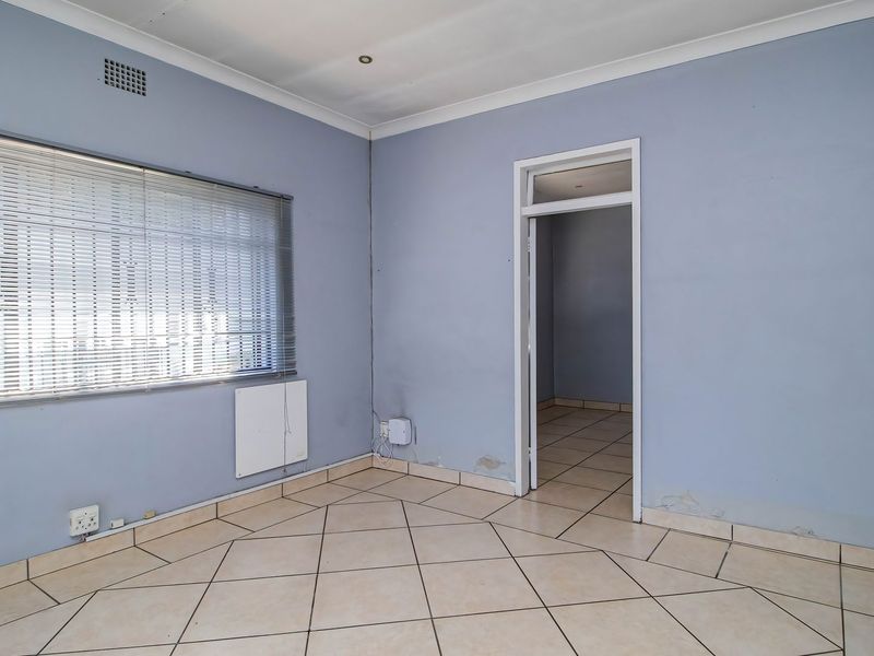 An empty office space featuring tiled flooring, venetian blinds, and recessed lighting, requiring minor wall repairs and cosmetic updates.