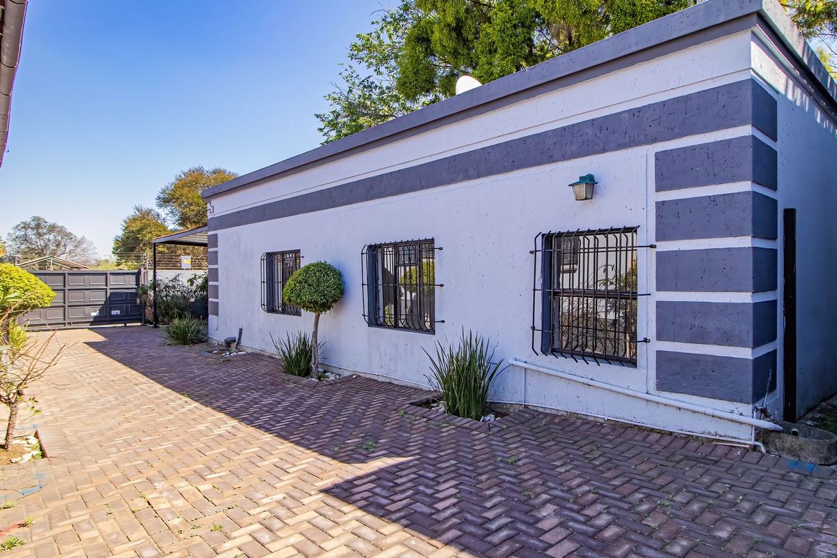Rear exterior view of the commercial property featuring a paved driveway, security-barred windows, and painted masonry walls.