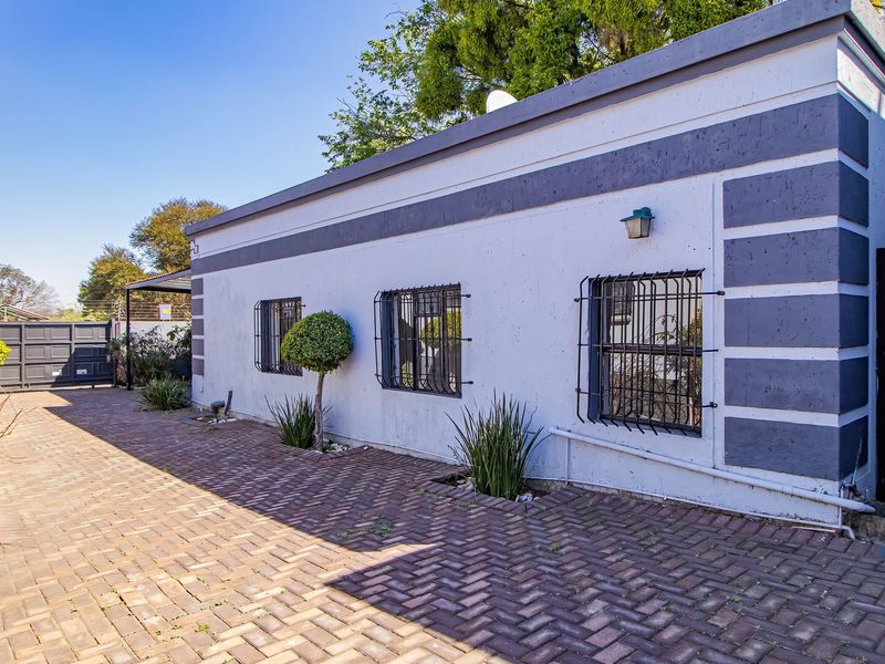 Rear exterior view of the commercial property featuring a paved driveway, security-barred windows, and painted masonry walls.