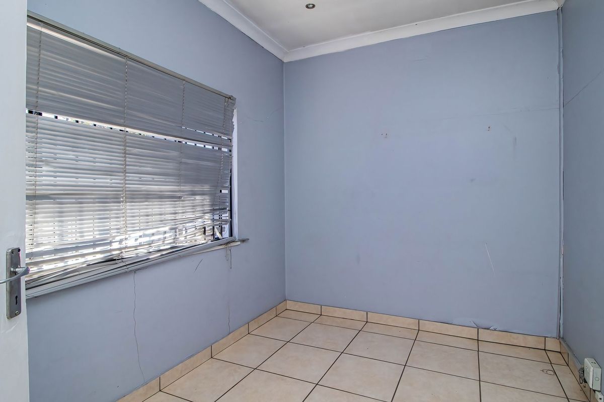An empty bedroom featuring tiled flooring, recessed downlights, and a window with venetian blinds, requiring minor cosmetic repairs to the walls and window treatments.