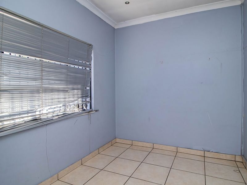 An empty bedroom featuring tiled flooring, recessed downlights, and a window with venetian blinds, requiring minor cosmetic repairs to the walls and window treatments.
