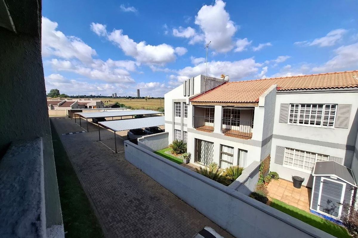 An elevated view of the rear exterior of the property, featuring a paved driveway, carport, small garden, and a balcony.