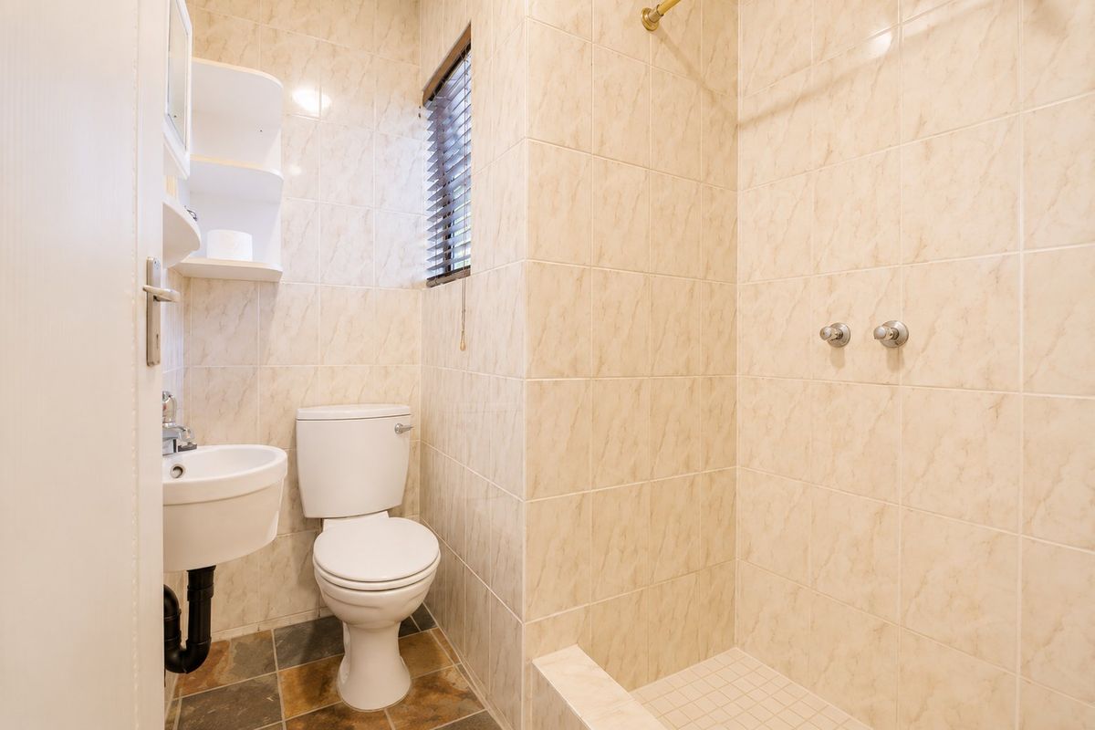 Compact bathroom featuring a walk-in shower, wall-mounted basin, and toilet with neutral tiled finishes and a small window.