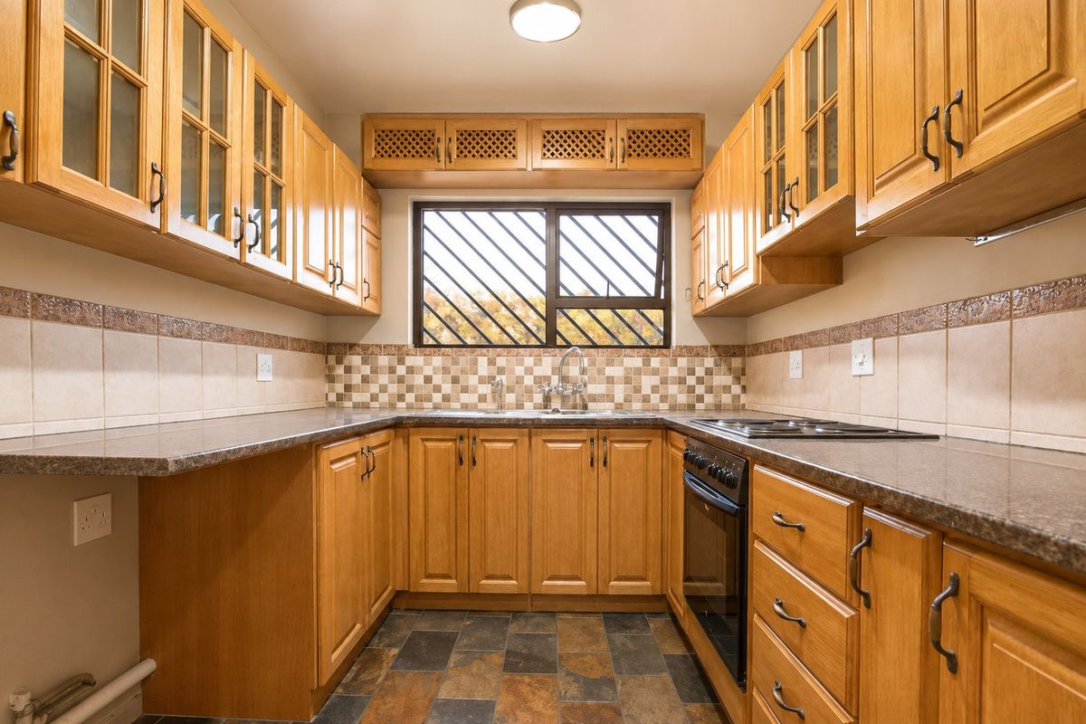 A functional galley-style kitchen featuring wooden cabinetry, granite-look countertops, a built-in oven and hob, and tiled splashbacks.