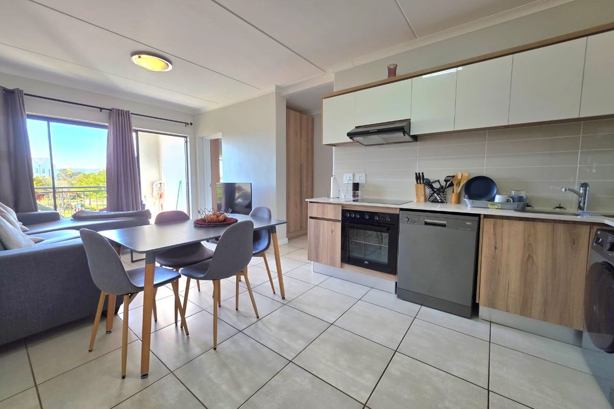 Modern open-plan living area featuring a contemporary kitchen with built-in cabinetry, integrated appliances, and tiled flooring, leading to a balcony with natural light.