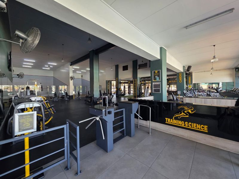 A spacious, well-maintained commercial gym facility featuring a reception area, secure turnstile access, and dedicated zones for cardio and circuit training.