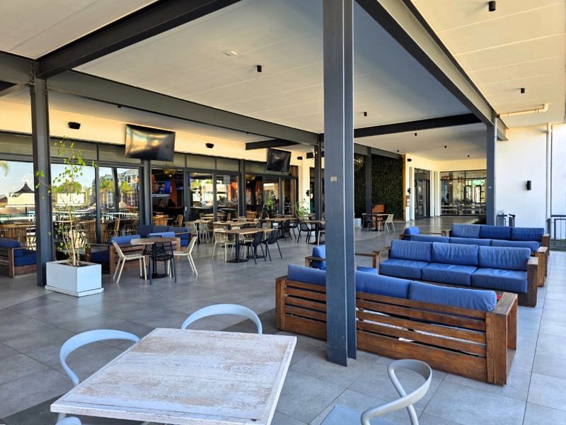 A spacious, covered outdoor patio area featuring tiled flooring, steel structural columns, and large sliding glass doors, ideal for alfresco dining and relaxation.