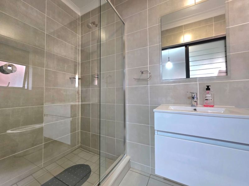 Modern bathroom featuring a glass-enclosed shower, wall-mounted vanity with integrated basin, and neutral ceramic tiling throughout.