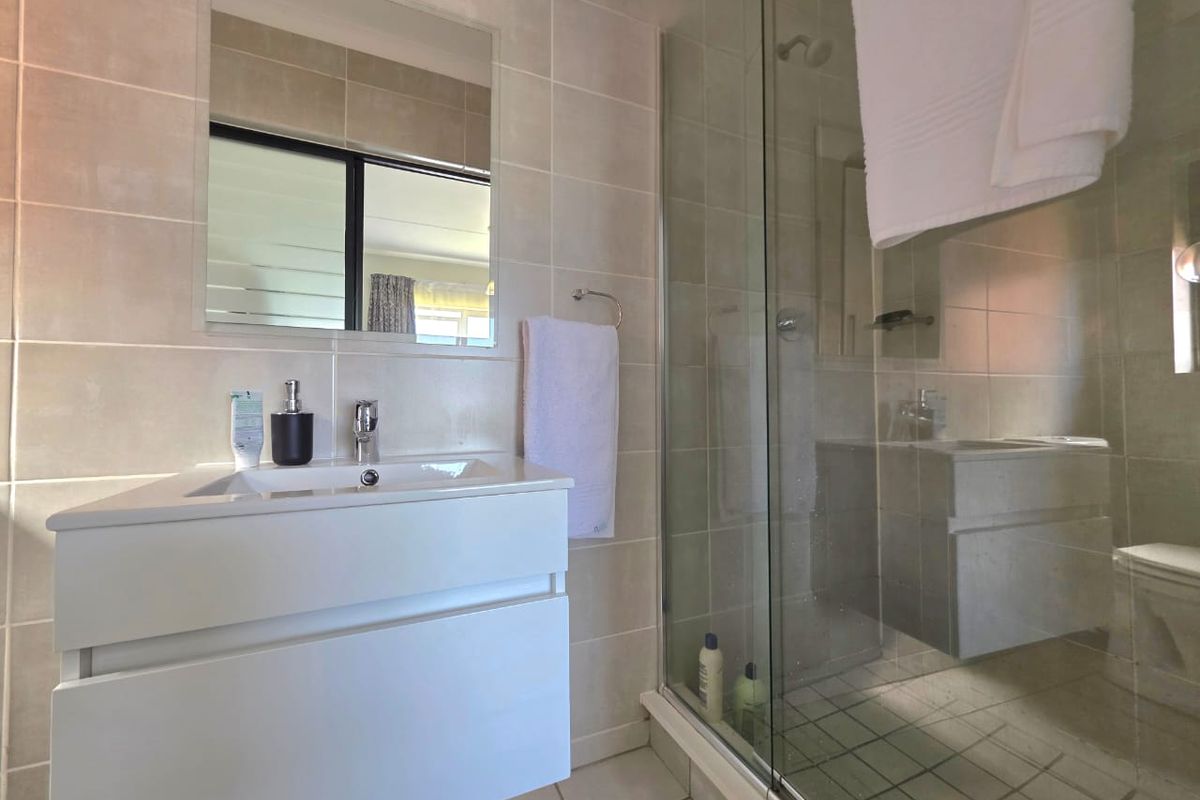 Modern bathroom featuring a wall-mounted vanity with basin, large mirror, and a spacious glass-enclosed shower with neutral ceramic tiling throughout.