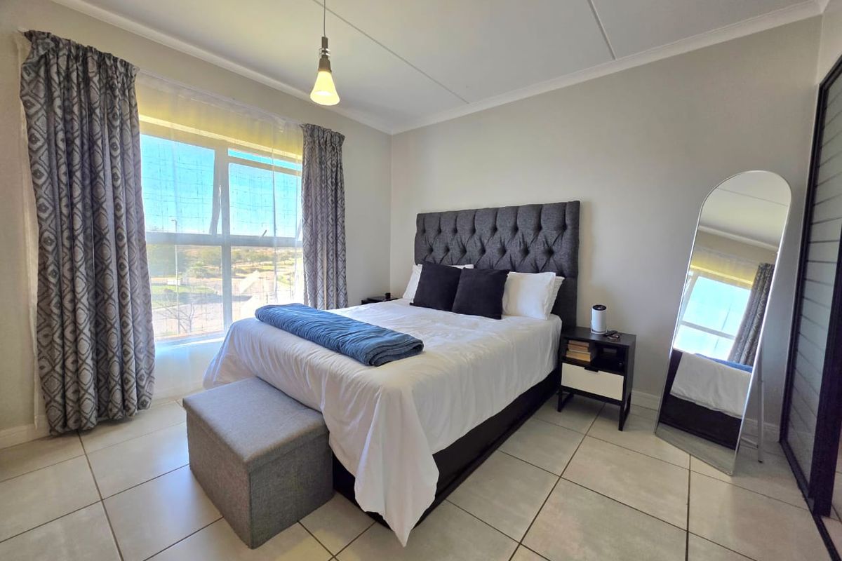 A well-lit bedroom featuring neutral tiled flooring, a large window with natural light, and built-in wardrobe storage.