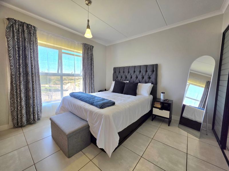 A well-lit bedroom featuring neutral tiled flooring, a large window with natural light, and built-in wardrobe storage.