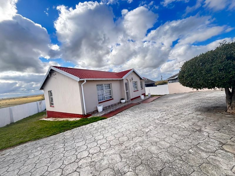 A well-maintained single-story house featuring a red tiled roof, paved driveway, and secure perimeter walling in a clear, open setting.