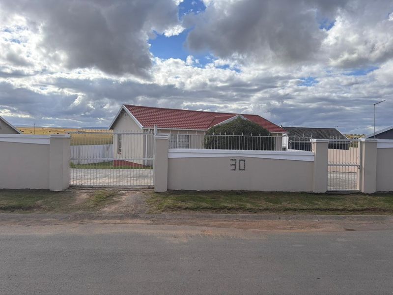 Front view of a residential property featuring a secure perimeter wall, metal driveway gate, and a tiled roof.