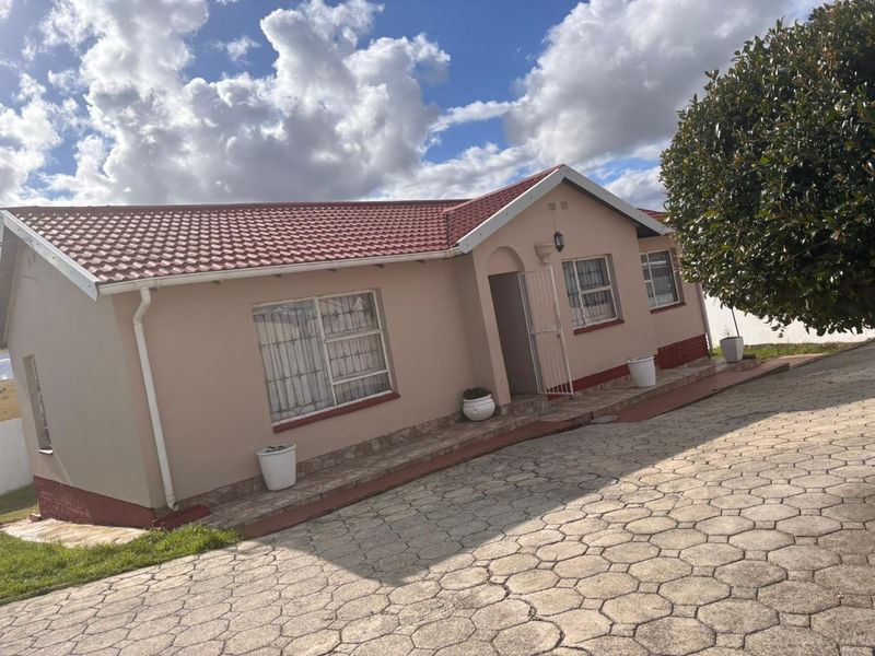 A well-maintained single-story residential home featuring a tiled roof, paved driveway, and secure window bars, set in a neat exterior environment.