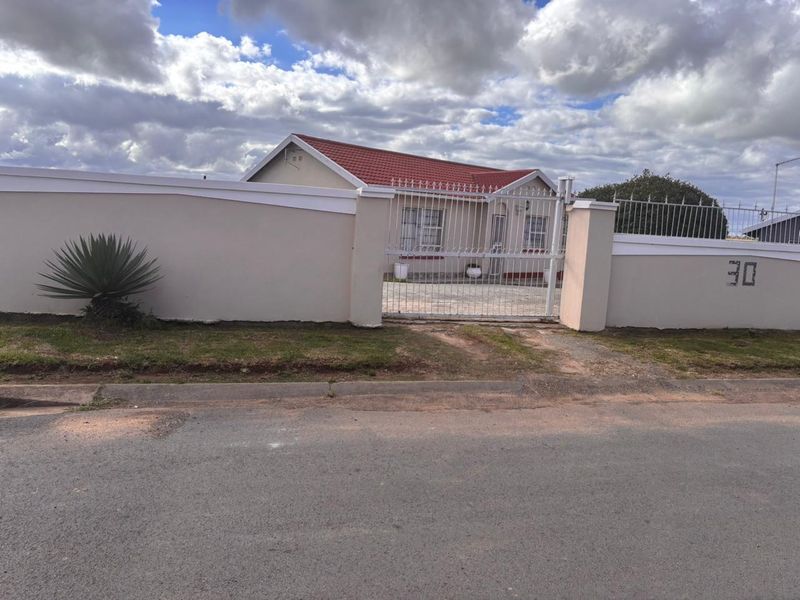 Front view of a residential property featuring a perimeter wall, metal security gate, and a tiled roof with a paved driveway.