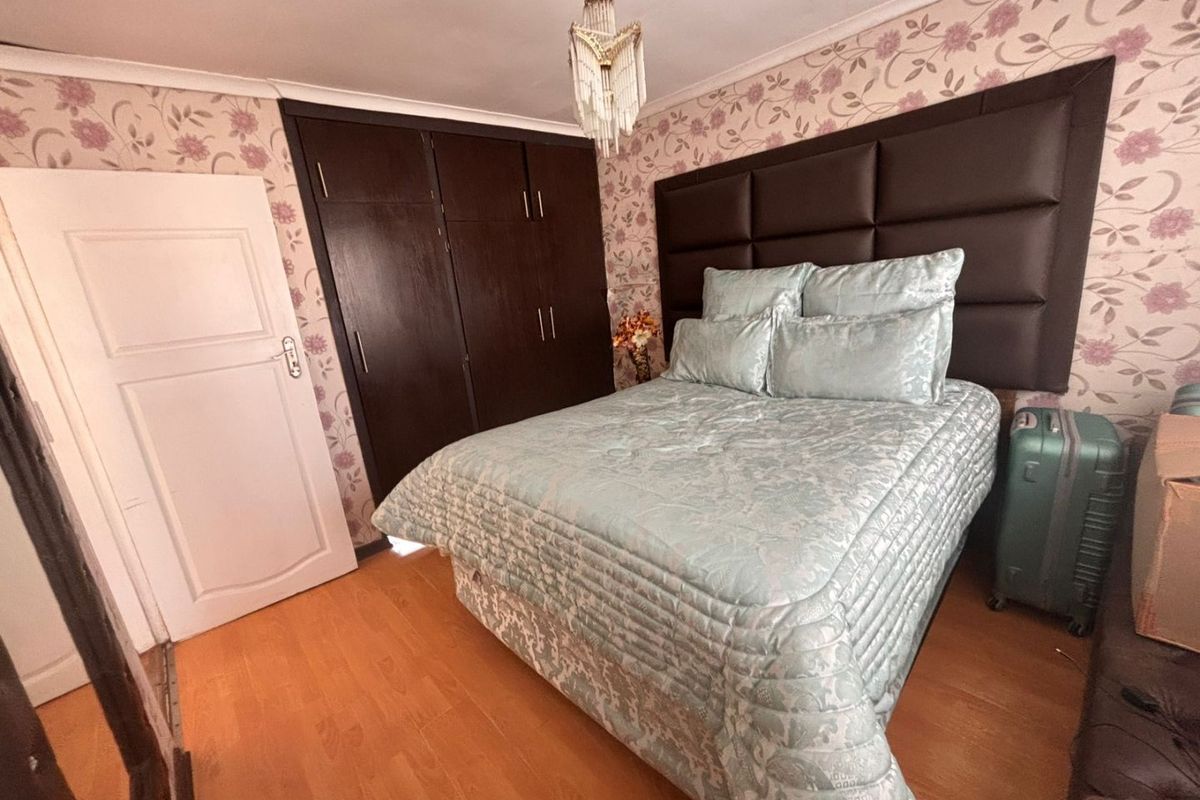 A bedroom featuring laminate flooring, built-in dark wood cupboards, and decorative floral wallpaper.