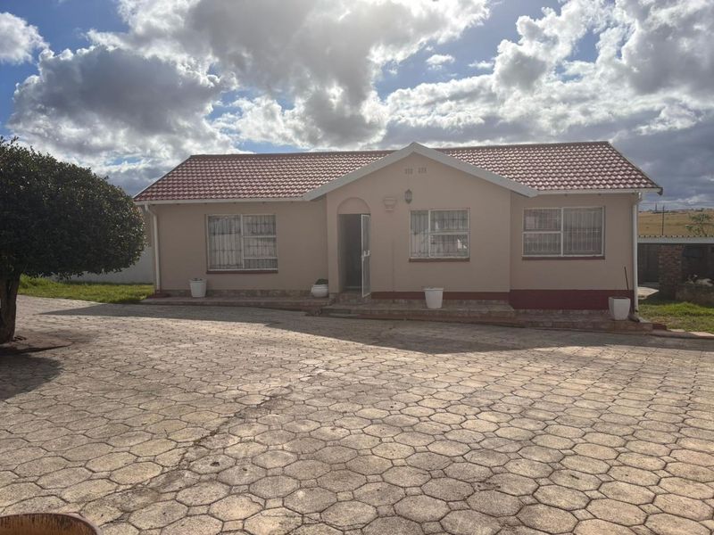 Front view of a single-story house featuring a tiled roof, brick facade, and a large paved driveway area.