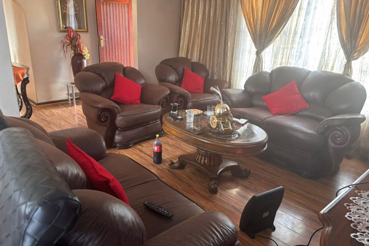 A living room featuring laminate flooring and large windows with curtains, providing a functional space for relaxation.