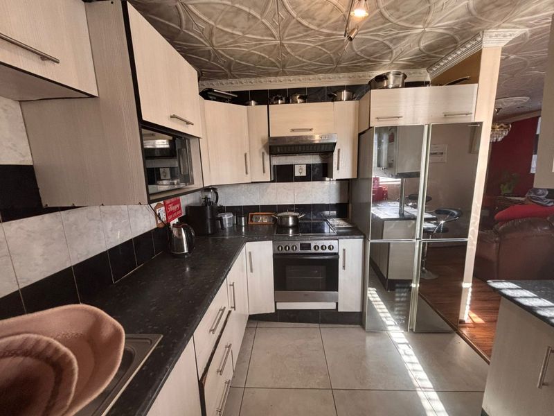 A functional kitchen featuring built-in cabinetry, dark laminate countertops, integrated oven and hob, and decorative ceiling tiles.