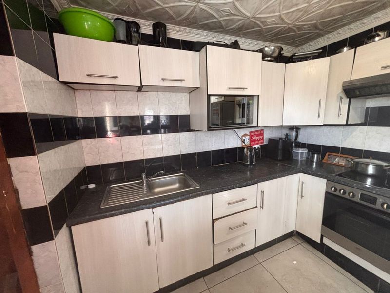 A functional kitchen featuring built-in cabinetry, a stainless steel sink, integrated oven, and cooktop with a tiled backsplash and floor.