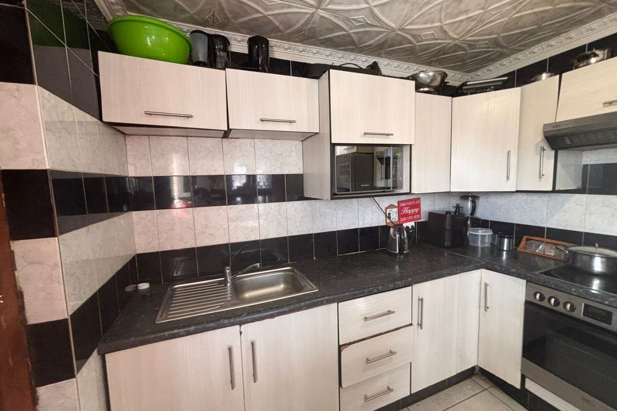 A functional kitchen featuring light-toned cabinetry, contrasting black and white tiled backsplash, stainless steel sink, and built-in oven with extractor fan.