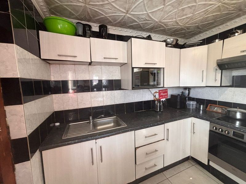 A functional kitchen featuring light-toned cabinetry, contrasting black and white tiled backsplash, stainless steel sink, and built-in oven with extractor fan.