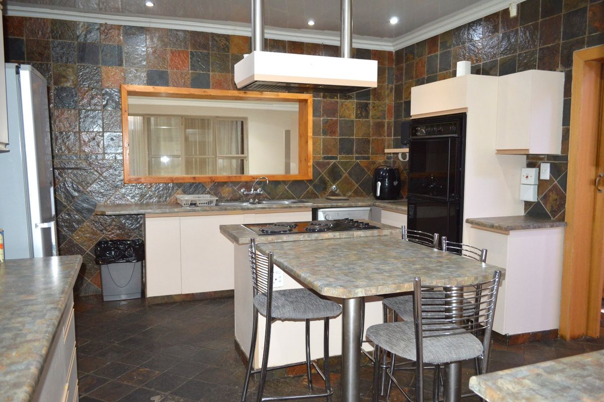 A functional kitchen featuring a central island with a gas hob, built-in oven, double sink, and extensive tiled splashbacks with ample cabinetry.