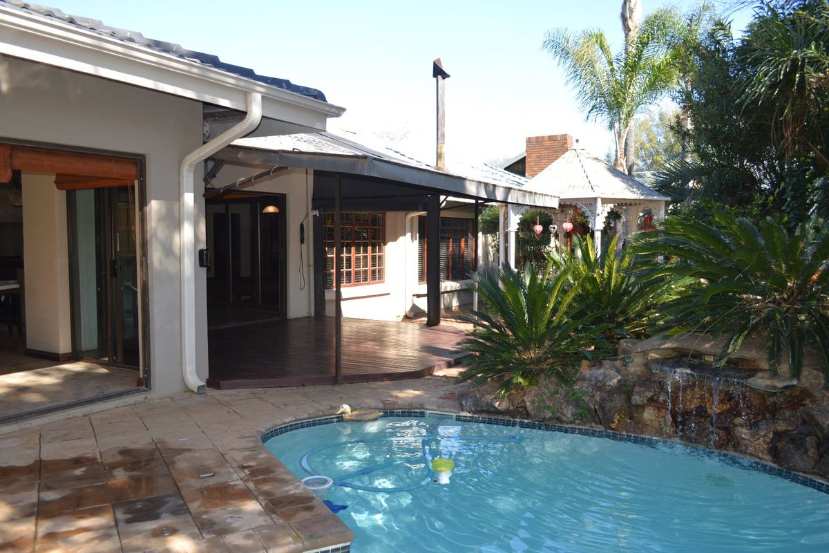 Rear exterior view featuring a swimming pool with a rock water feature, timber decking, and a covered patio area.