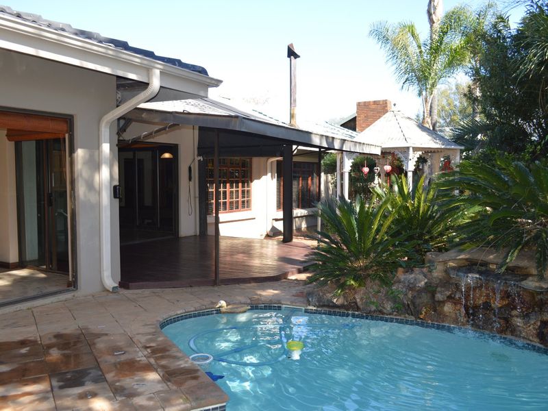 Rear exterior view featuring a swimming pool with a rock water feature, timber decking, and a covered patio area.