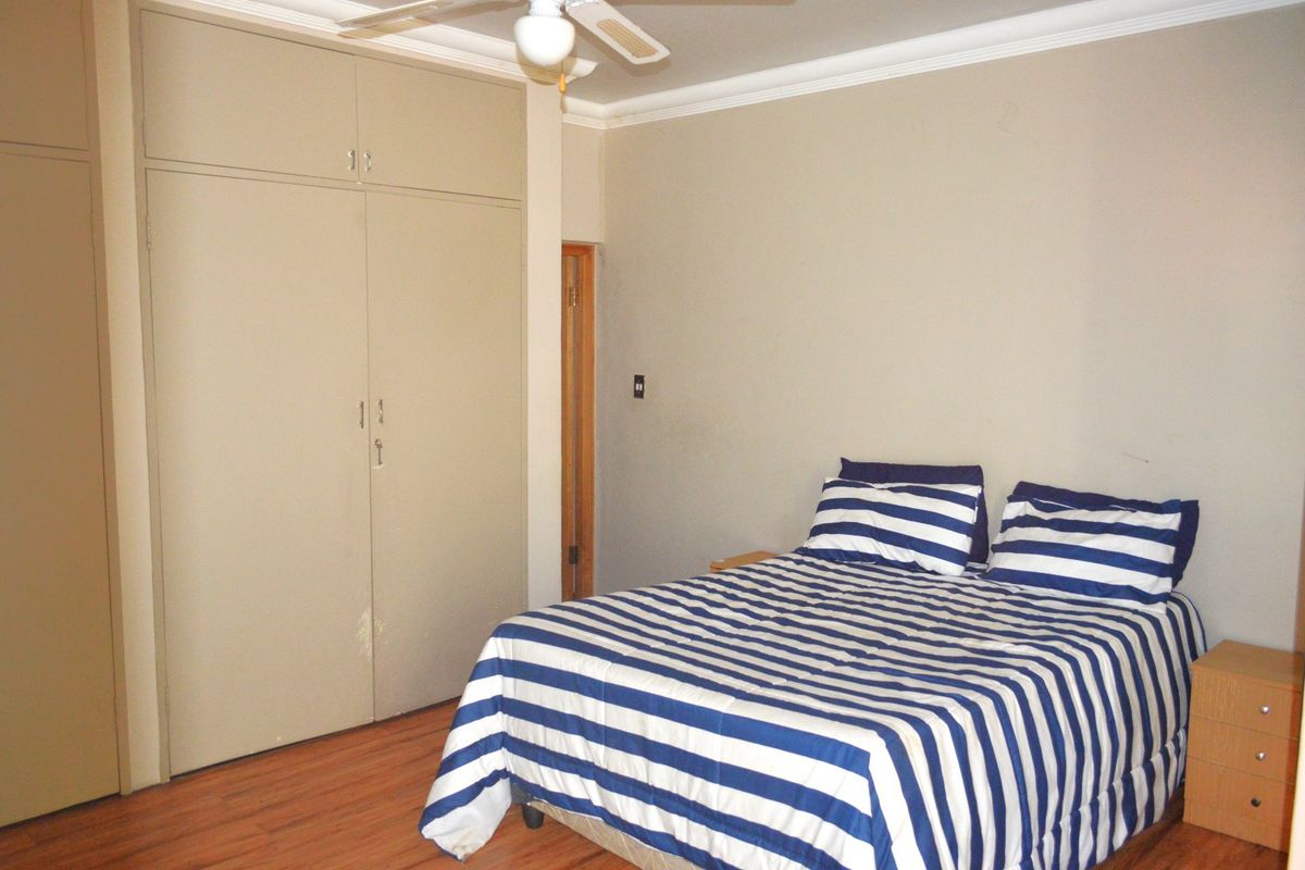 A functional bedroom featuring laminate flooring, a ceiling fan, and built-in cupboards providing ample storage space.