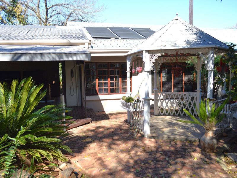 Rear exterior view featuring a paved patio area, a decorative gazebo, and solar water heating panels installed on the tiled roof.