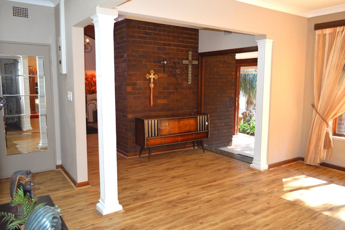 Living area featuring an exposed brick feature wall, laminate flooring, and decorative columns, providing a distinct architectural transition between spaces.