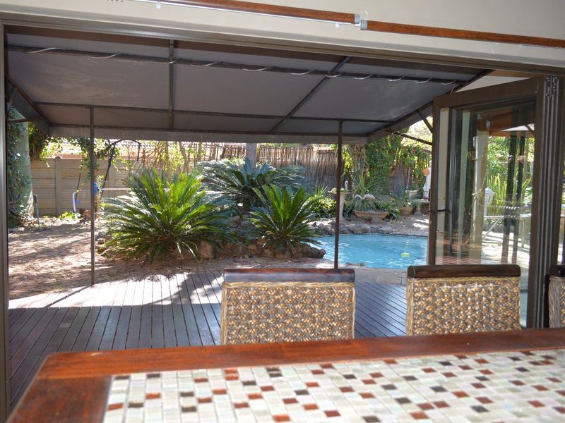 Covered timber deck patio overlooking a private swimming pool and landscaped garden area, providing a seamless transition between indoor and outdoor living spaces.
