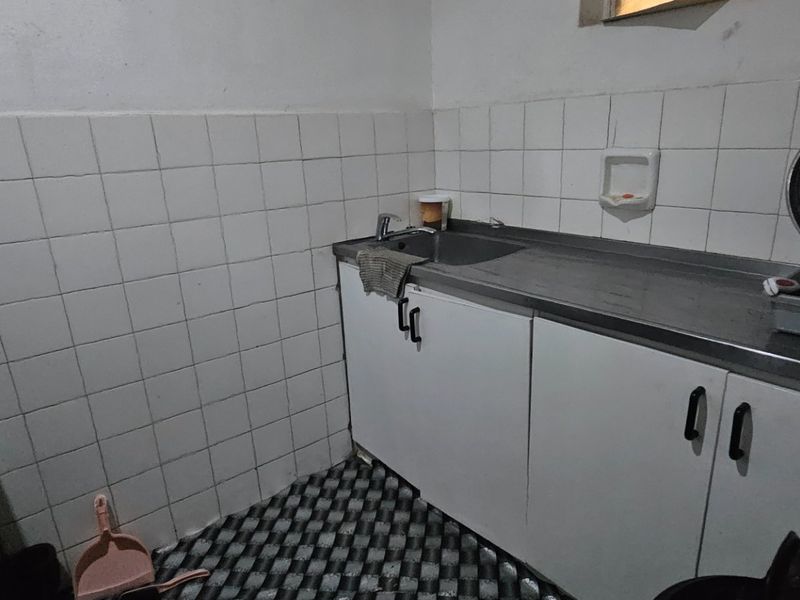 A compact kitchen featuring built-in cabinetry, a stainless steel sink, tiled splashback, and an electric stove, requiring cosmetic updates to modernize the space.