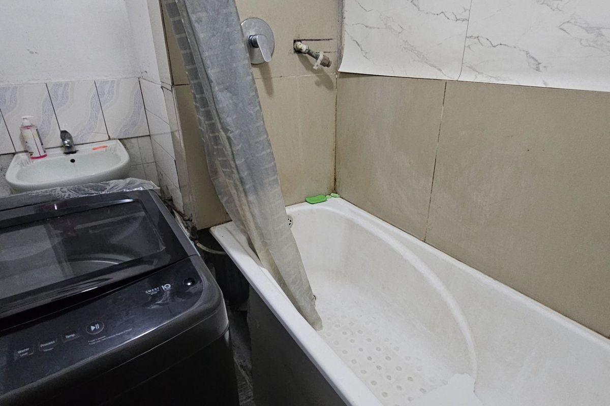 Compact bathroom featuring a bathtub, wall-mounted basin, and tiled walls. The space requires maintenance and finishing of plumbing fixtures.