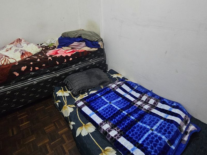 A compact bedroom featuring parquet flooring and plain walls, currently utilized with multiple beds.