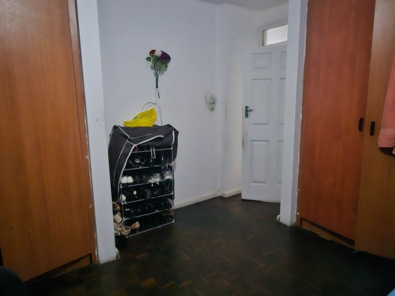 Bedroom featuring built-in wooden cupboards and dark parquet flooring, offering functional storage space in need of cosmetic updates.