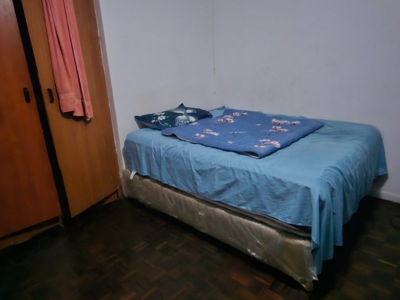 A compact bedroom featuring parquet flooring and a built-in wardrobe, requiring cosmetic updates to the wall finishes and general maintenance.
